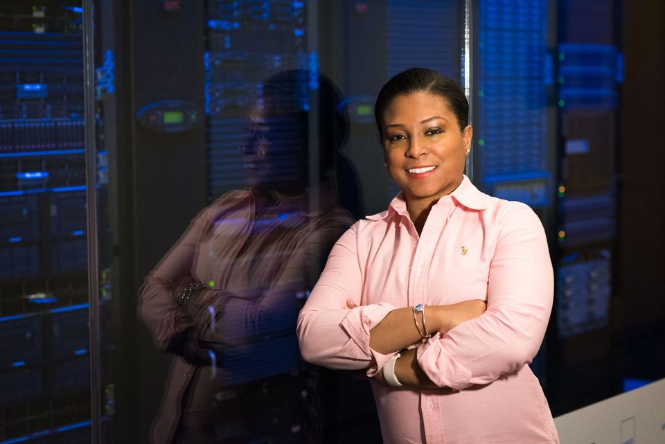 An IT professional standing with crossed arms in a server room, smiling